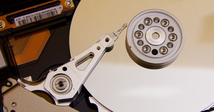 An image of the mechanical parts of a hard disk drive or HDD that features a rotating metallic magnetic disk and a magnetic read-write head.